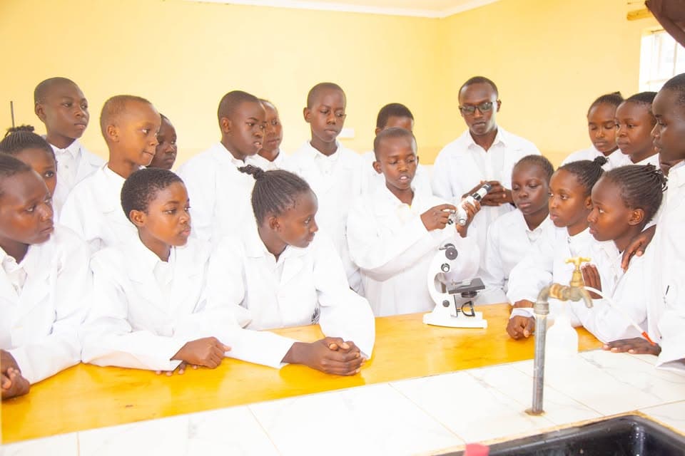 Students in white lab coats gather around a microscope during a science lesson in a laboratory.