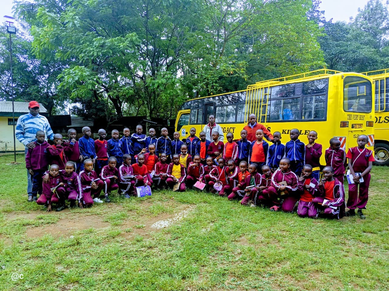 Students in maroon and blue uniforms pose for a photo before a yellow school bus.