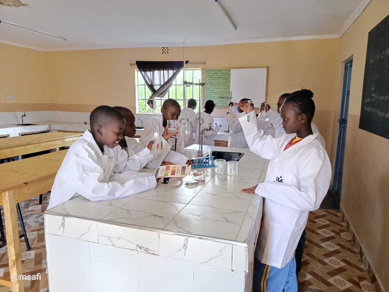 Young students in white lab coats perform science experiments with glassware in a classroom laboratory.