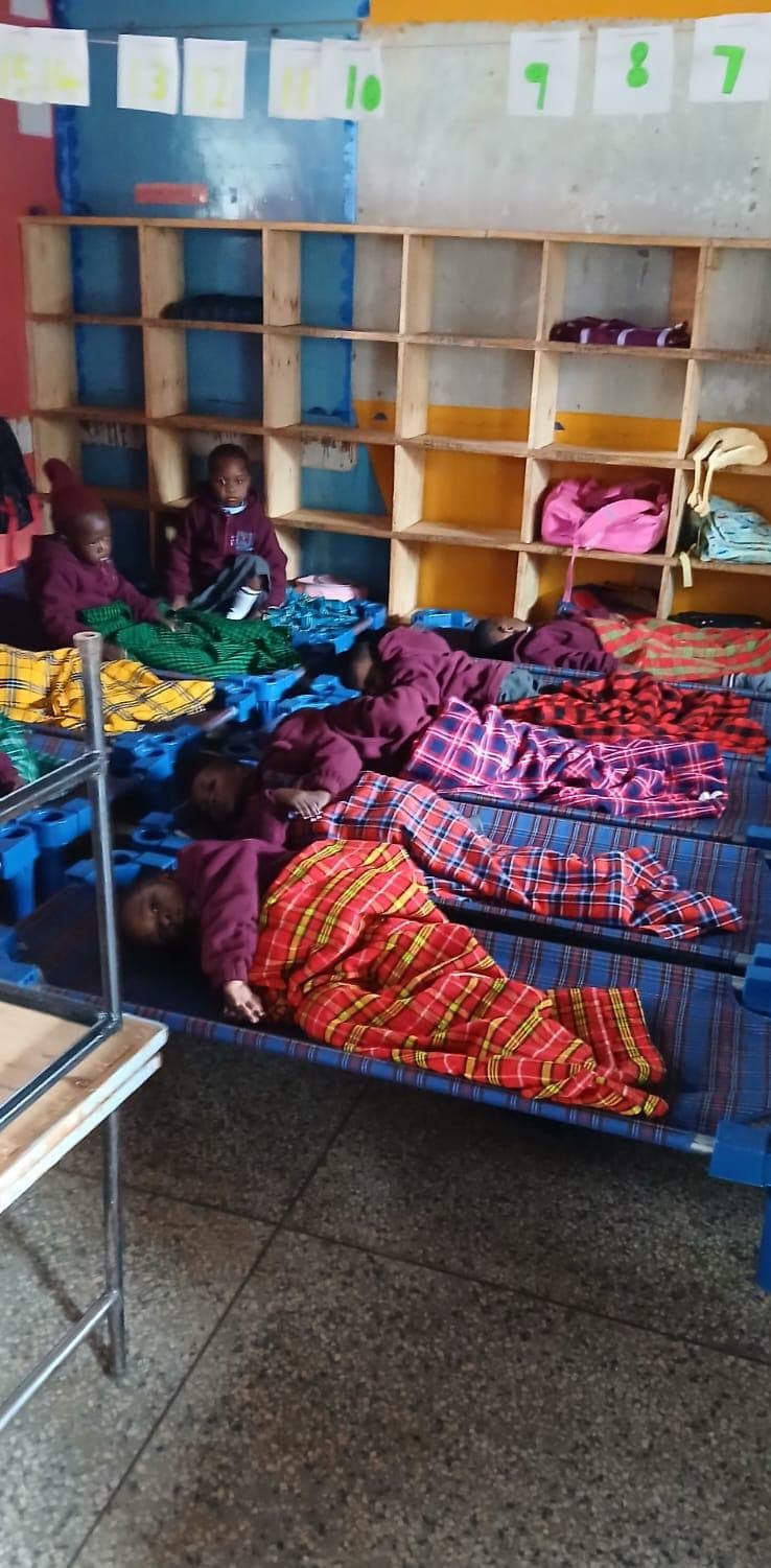 Young children nap on blue cots covered in colorful plaid blankets in a classroom setting.